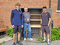  Former Edison students and their trade teacher pose in front of a shelving unit they built.